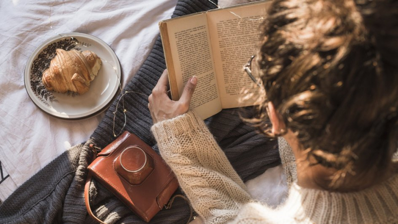 Молодая женщина читает книжку, лежа на диване 